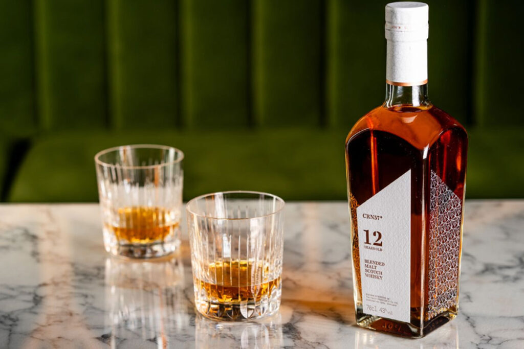 A bottle of CRN57 12 Years Old Blended Malt Scotch Whisky with two drams served in glasses next to the bottle. All of this is sitting on top of a marble tabletop.