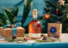 Canerock Rum brings the festive spirit to Sainsbury’s aisles A bottle of Canerock Rum sits in the middle of a table filling with Christmas decorations and wrapped presents with a Christmas tree in the background.