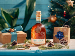Canerock Rum brings the festive spirit to Sainsbury’s aisles A bottle of Canerock Rum sits in the middle of a table filling with Christmas decorations and wrapped presents with a Christmas tree in the background.