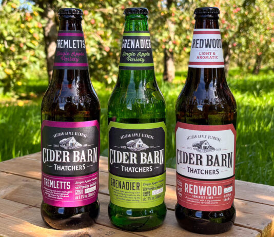 Thatchers expands Cider Barn range with a trio of new launches Thatchers Cider Barn bottles stand on a wooden crate in the middle of a grassy scene including Thatchers Redwood, Thatchers Grenadier and Thatchers Tremletts.