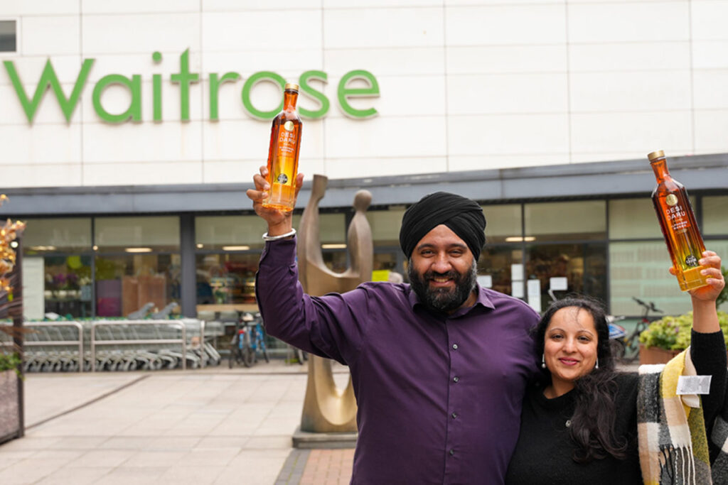 Desi Daru founders Mohit Singh and Aneet Kaur stand outside a Waitrose store holding bottles of Desi Daru Mango Vodka.
