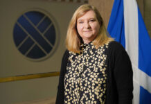 ScotGov publishes HFSS regulations Jenny Minto MSP, minister for public health and women's health, stands in Scottish Parliament with the Scotland flag behind her.