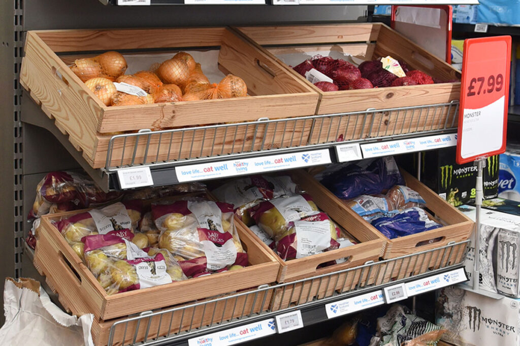 Wooden boxes holding fruit and vegetables sit on top of a store shelf unit.