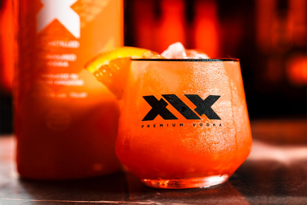 A promotional image for the XIX Vodka brand with a cocktail serve in a XIX branded glass with a bottle of the vodka behind the glass.