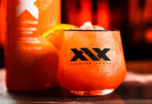 XIX Vodka expands distribution with Red Star Brands partnership A promotional image for the XIX Vodka brand with a cocktail serve in a XIX branded glass with a bottle of the vodka behind the glass.