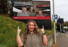 Coca-Cola donates £120k to communities chosen by ‘The Bosses’ Sophie Williams, retailer at Premier Broadway Convenience Store, stands in front of a billboard as part of the 'The Bosses' campaign. The billboard includes an image of Sophie and her parents inside their store.