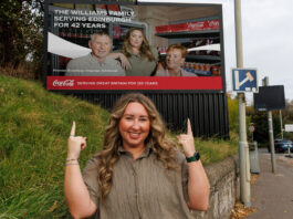 Coca-Cola donates £120k to communities chosen by ‘The Bosses’ Sophie Williams, retailer at Premier Broadway Convenience Store, stands in front of a billboard as part of the 'The Bosses' campaign. The billboard includes an image of Sophie and her parents inside their store.