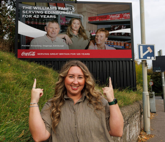 Coca-Cola donates £120k to communities chosen by ‘The Bosses’ Sophie Williams, retailer at Premier Broadway Convenience Store, stands in front of a billboard as part of the 'The Bosses' campaign. The billboard includes an image of Sophie and her parents inside their store.