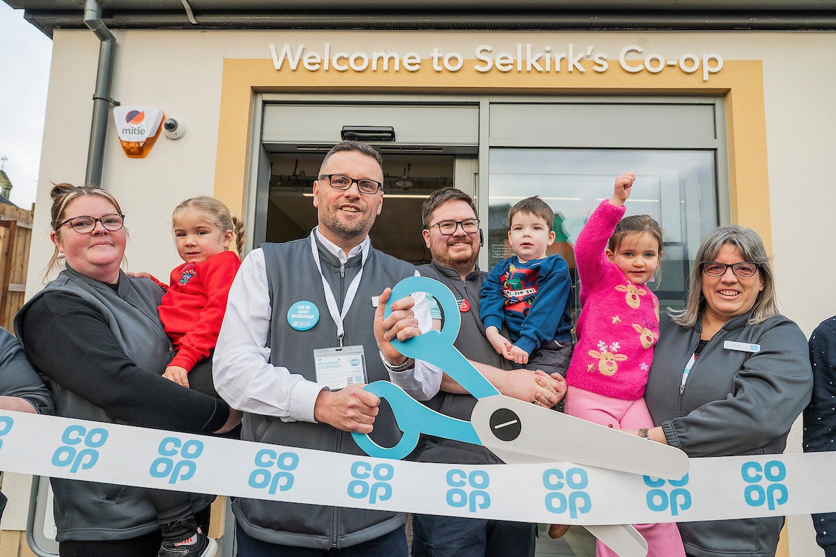 A group of people open Co-op Selkirk using novelty scissors to cut a Co-op branded ribbon.