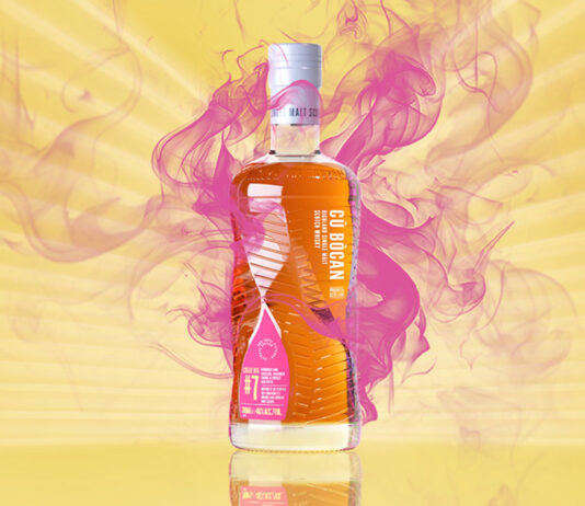 Cù Bòcan marks 20 years at Tomatin with new whisky A bottle of Cù Bòcan Creation #7 stands against a yellow background with lines of light coming from the centre and pink smoke behind the bottle.