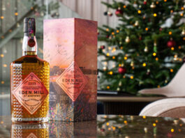 Eden Mill unveils new Art of St Andrews whisky A bottle of Eden Mill Art of St Andrews 2025 single malt stands on a table with its outer packaging next to it with a Christmas tree in the background.