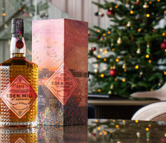 Eden Mill unveils new Art of St Andrews whisky A bottle of Eden Mill Art of St Andrews 2025 single malt stands on a table with its outer packaging next to it with a Christmas tree in the background.