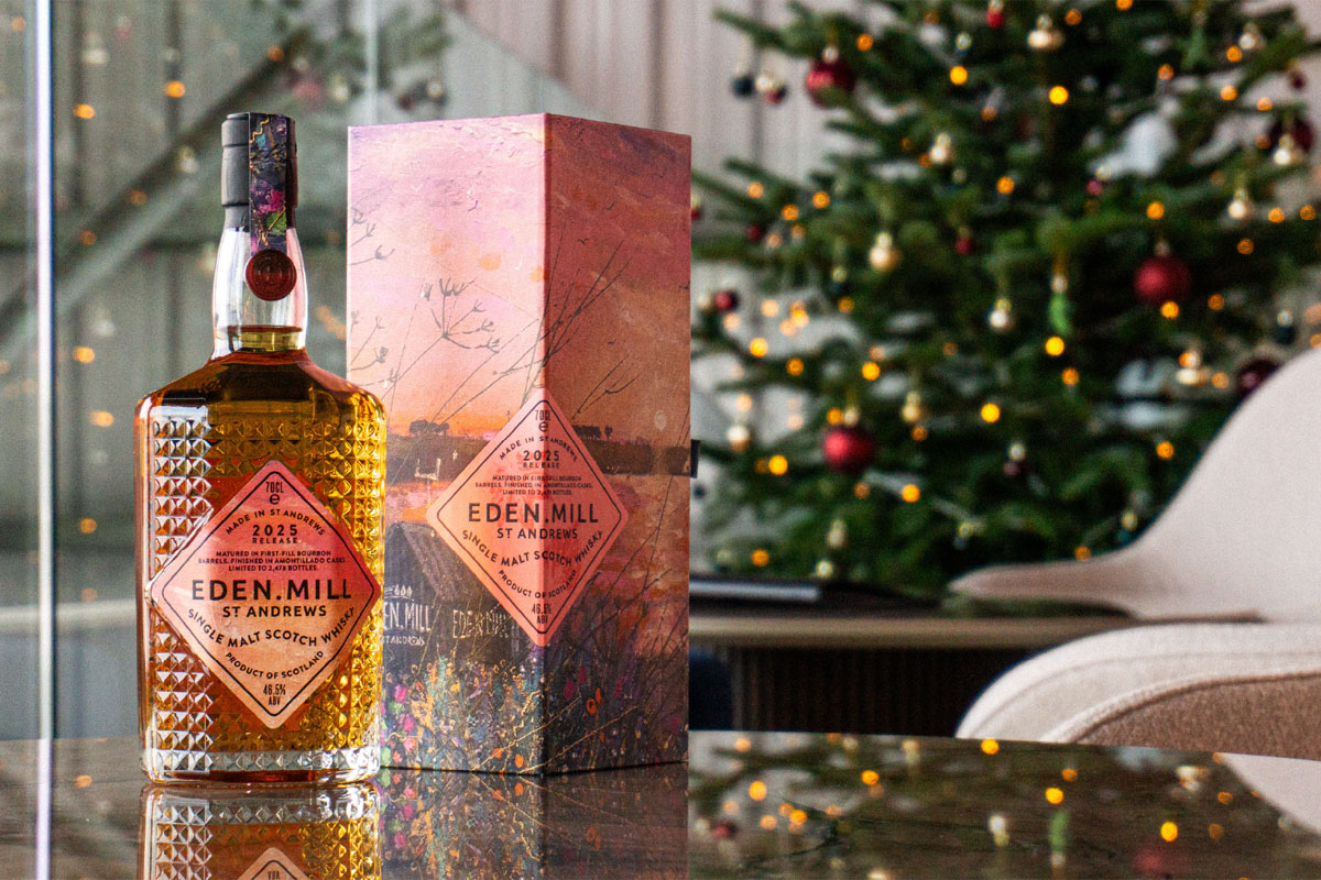 A bottle of Eden Mill Art of St Andrews 2025 single malt stands on a table with its outer packaging next to it with a Christmas tree in the background.