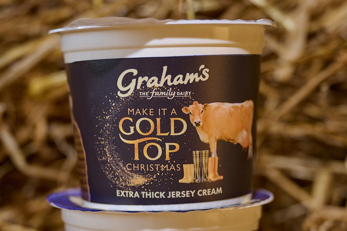 A pack of Graham's Gold Top Extra Thick Jersey Cream stands on top of another pack in a barn with straw behind it.