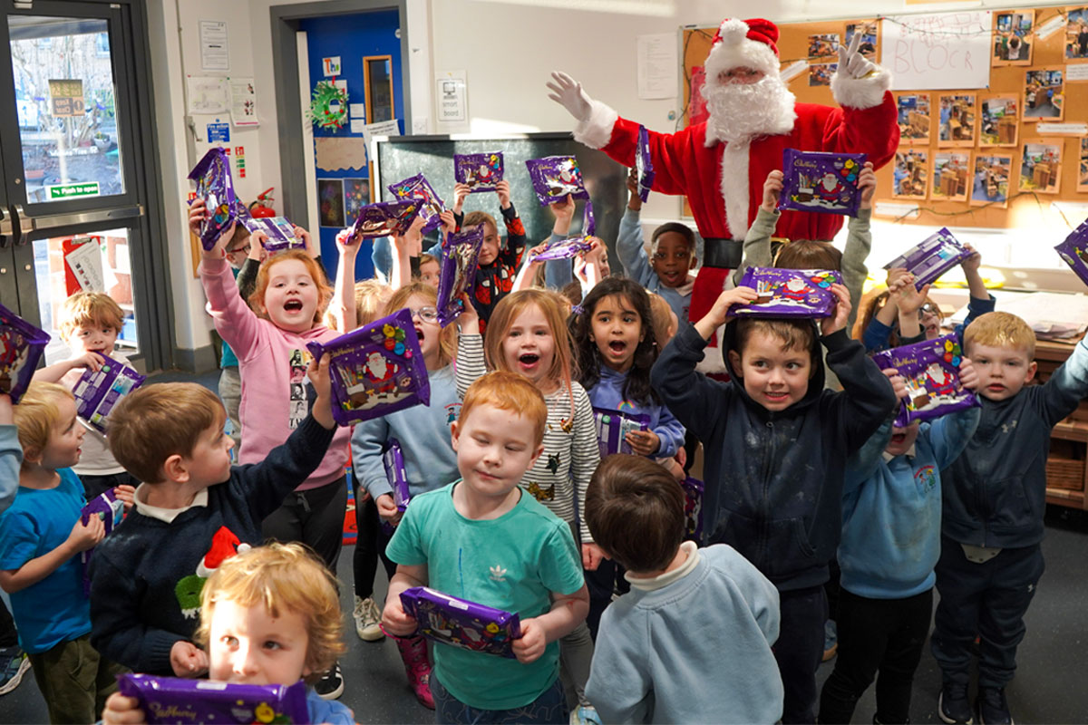 A group of children celebrate holding Cadbury Christmas Selection boxes with Santa Claus celebrating with them.