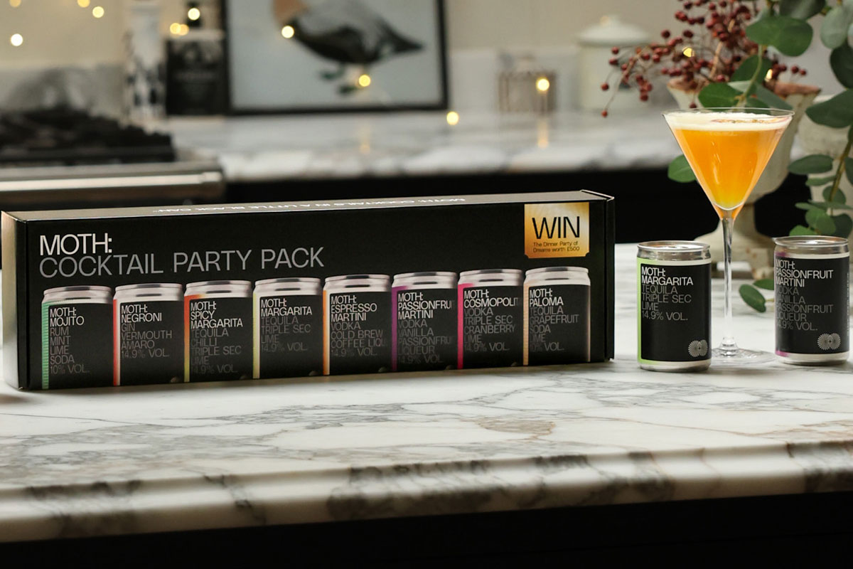 The Moth Cocktail Party Pack stands on a kitchen counter with cans of the cocktails next to it and a cocktail serve in a glass.