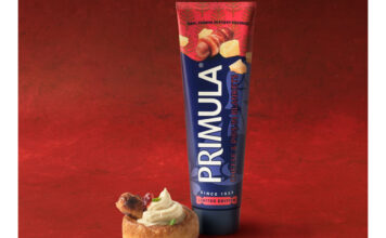 Primula brings back festive Pigs in Blankets flavour A tube of Primula Cheese Pigs in Blankets flavour stands next to a small bite serve using the cheese. This is against a red velvet background.