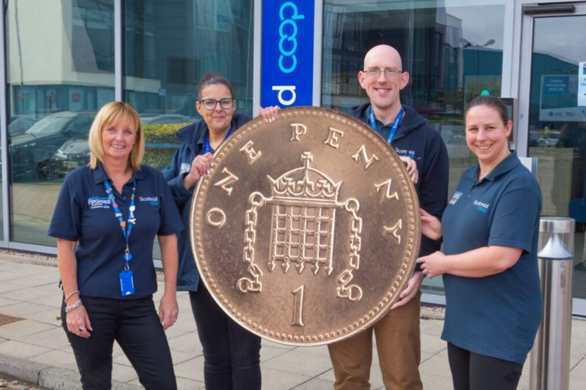 Members of the Scotmid team stand together holding a novelty sized penny coin in front of the firm's headquarters.