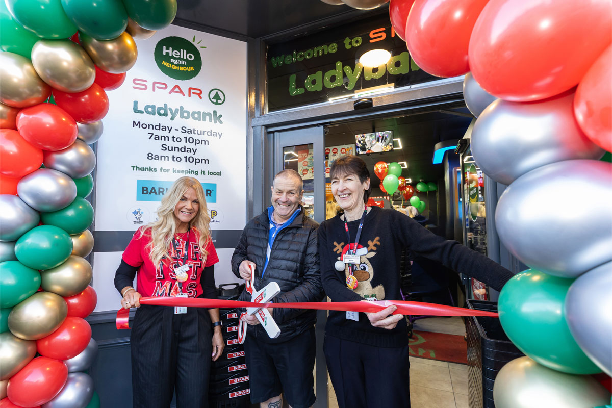 A group of people stand at the entrance to Spar Market Ladybank whilst cutting a ribbon with a novelty pair of scissors.