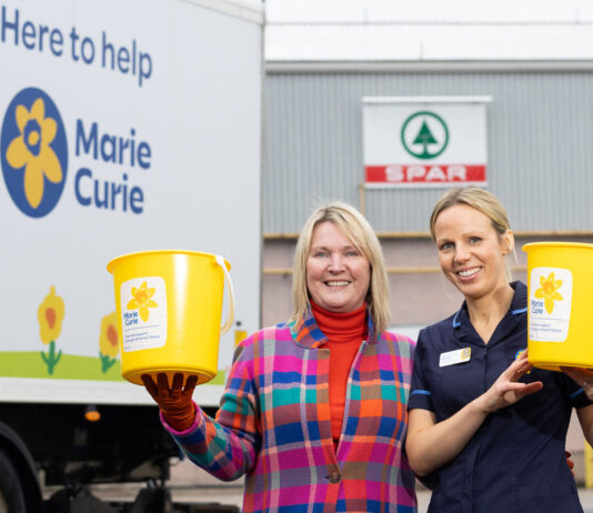 Spar Scotland hits record-breaking fundraising for charity Two staff members stands the Spar Scotland wholesale depot holding fundraising buckets for Marie Curie with the charity's branded van behind them.