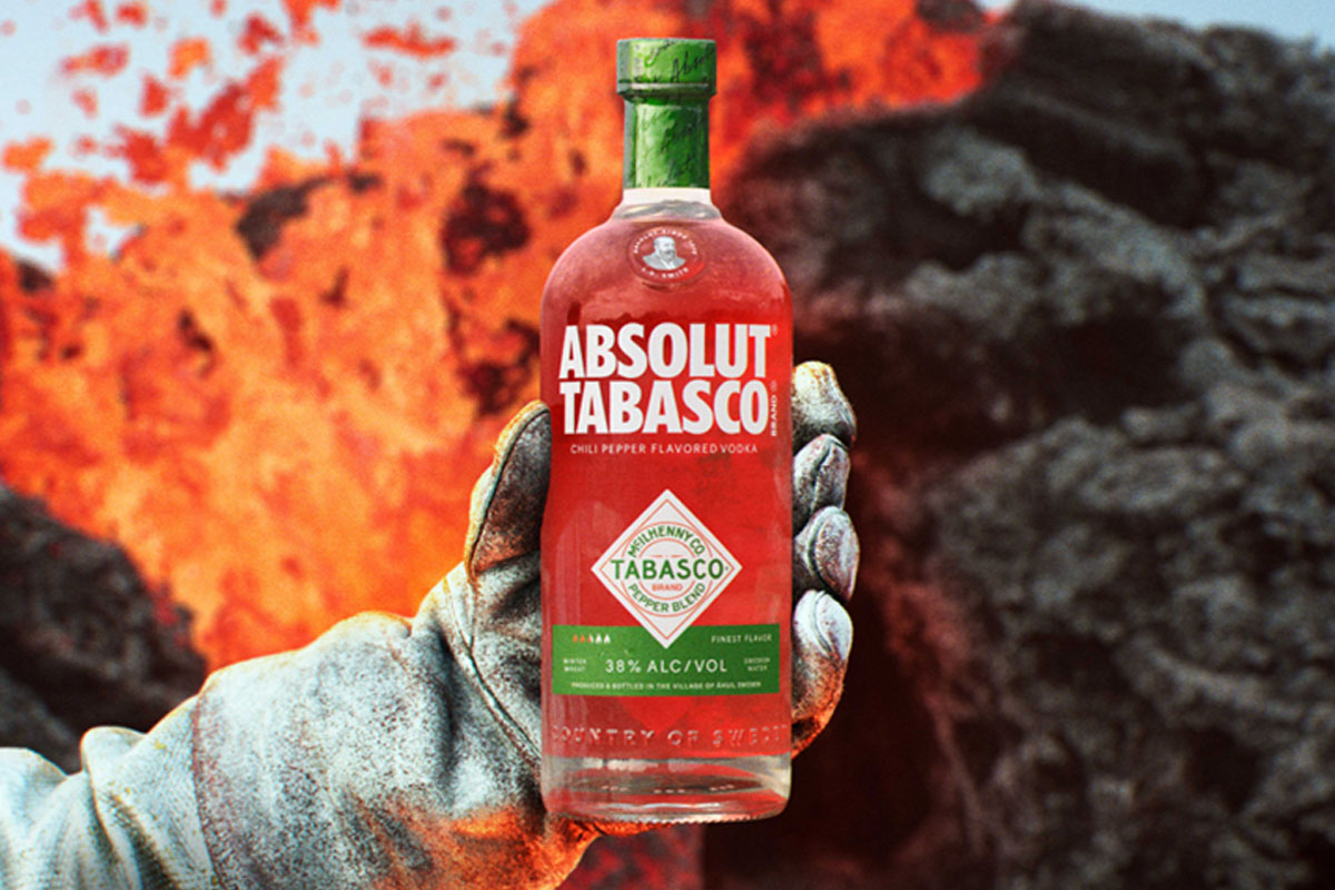 A person holds a bottle of Absolut Tabasco Vodka with an insulated gloved hand against the background of an erupting volcano.