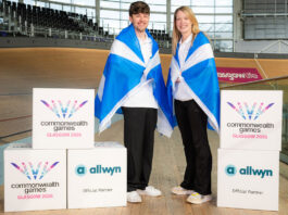 Allwyn announced as partner for Glasgow Commonwealth Games Two people stand in the Sir Chris Hoy Velodrome with Scotland flags draped across their shoulders with decorative boxes that have the Glasgow 2026 Commonwealth Games and Allwyn logos on them.