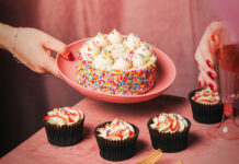 Finsbury launches first-to-market cake bento boxes A person places a large celebration cake on a pink plate down onto a table that already has four cupcakes sitting on it.