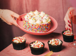 Finsbury launches first-to-market cake bento boxes A person places a large celebration cake on a pink plate down onto a table that already has four cupcakes sitting on it.