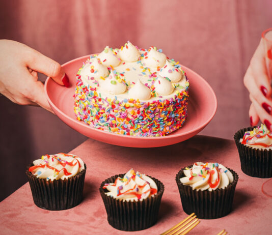 Finsbury launches first-to-market cake bento boxes A person places a large celebration cake on a pink plate down onto a table that already has four cupcakes sitting on it.
