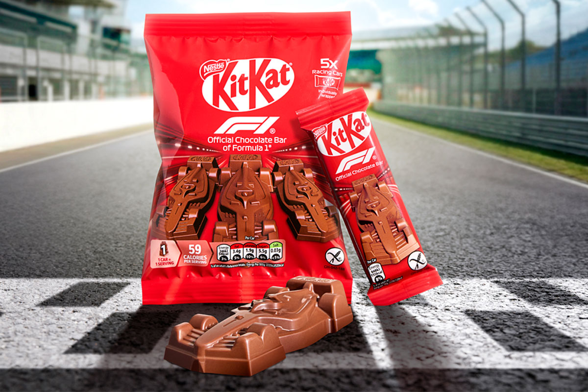 A pack of KitKat Formula 1 Chocolate Cars as well as a single pack and a chocolate car out of its pack sit on a finish line on a racetrack.