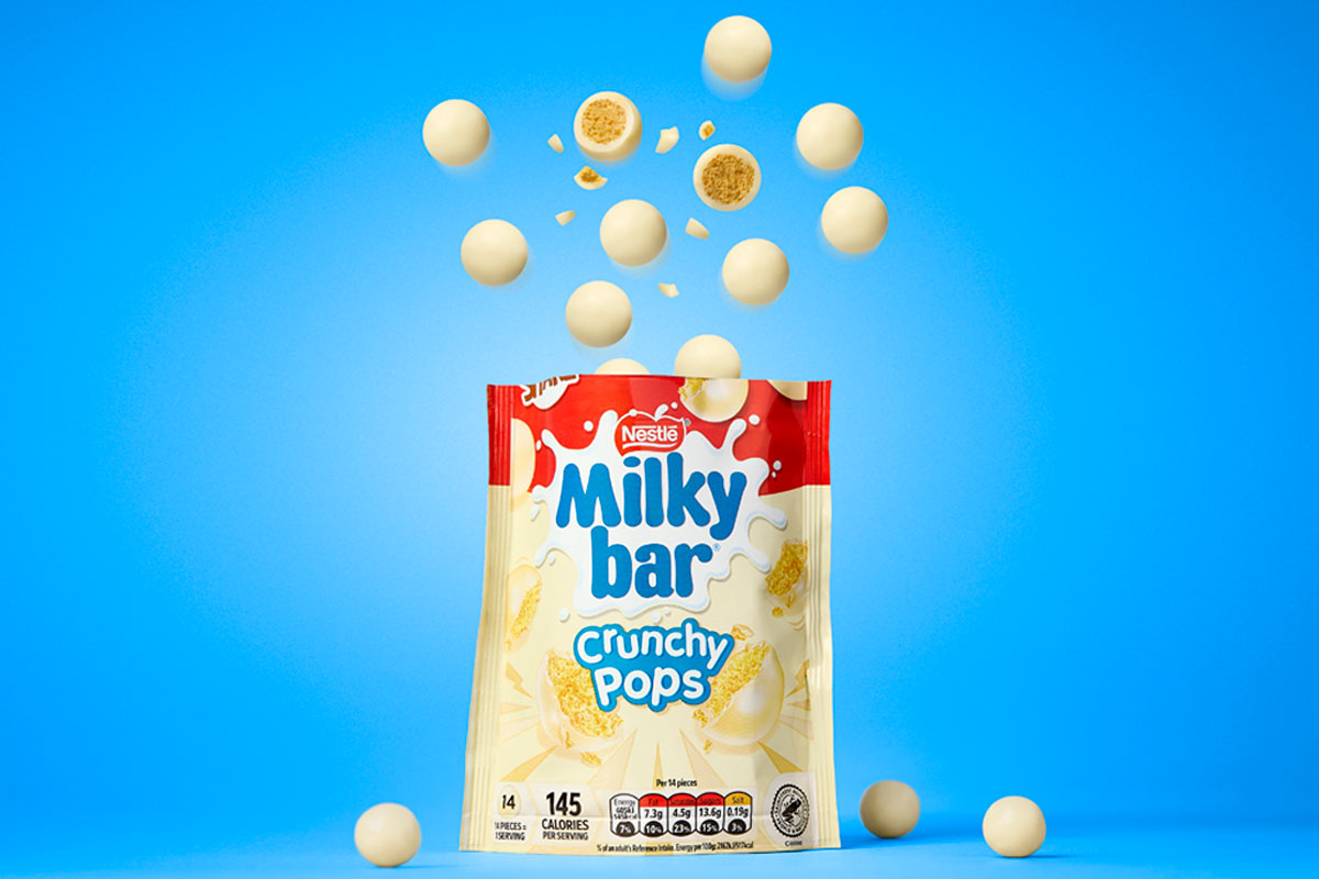 A packet of Milkybar Crunchy Pops stands open against a blue background with pieces of the chocolate rising out of the top of the bag.