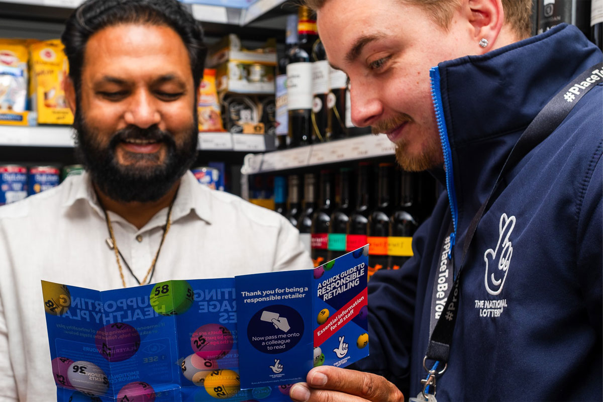 A representative of the National Lottery shows a retailers a pamphlet for the National Lottery inside his store.