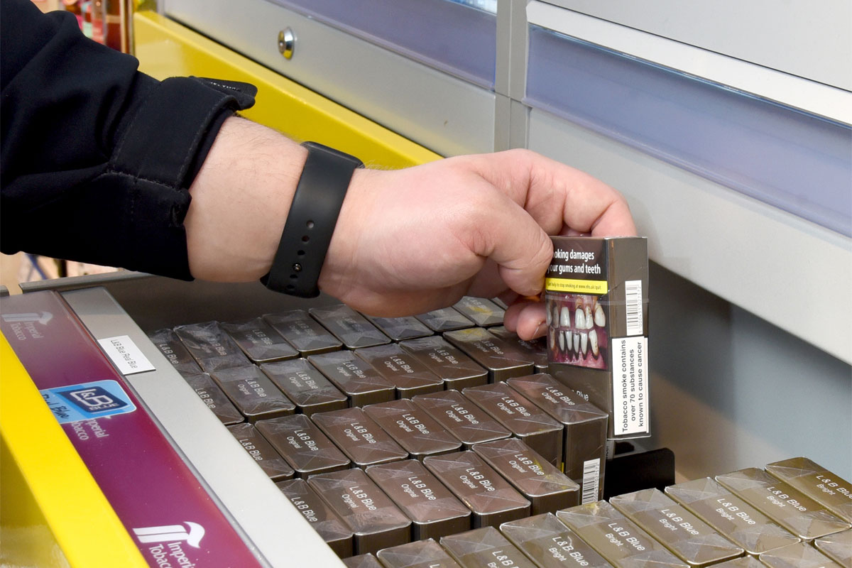 A person is lifting out a pack of cigarettes from a drawer at the back of a shop.