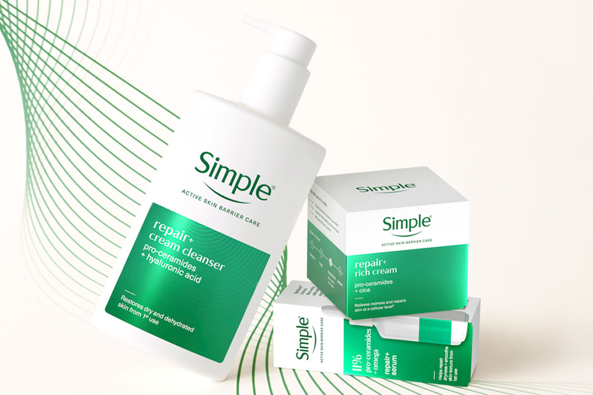 A bottle of Simple Repair+ Cream Cleanser leans on packs of Simple Repair+ Rich Cream and Simple Repair+ Serum against a white background with green design elements.