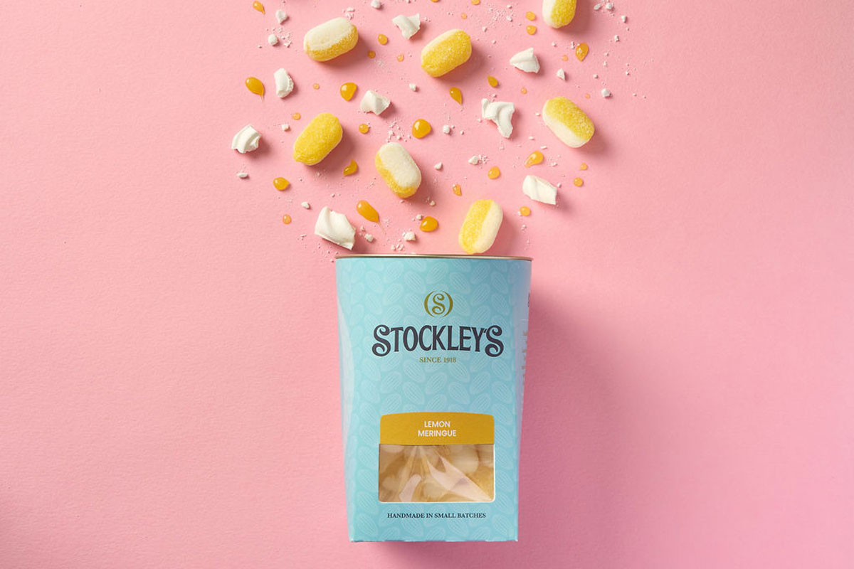 A pack of Stockley's Lemon Meringue hard-bolied sweets is tipped out over a pink background with the sweets spilling out.