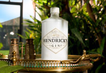 Hendrick’s grows core range with Another Hendrick’s gin A bottle of Another Hendrick's Gin sits on a golden tabletop in a glass greenhouse with greenery around it.
