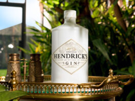 Hendrick’s grows core range with Another Hendrick’s gin A bottle of Another Hendrick's Gin sits on a golden tabletop in a glass greenhouse with greenery around it.
