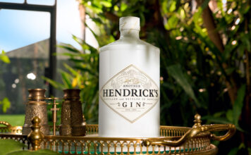 Hendrick’s grows core range with Another Hendrick’s gin A bottle of Another Hendrick's Gin sits on a golden tabletop in a glass greenhouse with greenery around it.