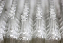 Glass bottle returns permitted under Welsh DRS Rows of glass bottles are lined up on a conveyer belt.