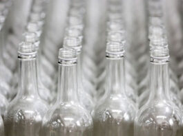 Glass bottle returns permitted under Welsh DRS Rows of glass bottles are lined up on a conveyer belt.