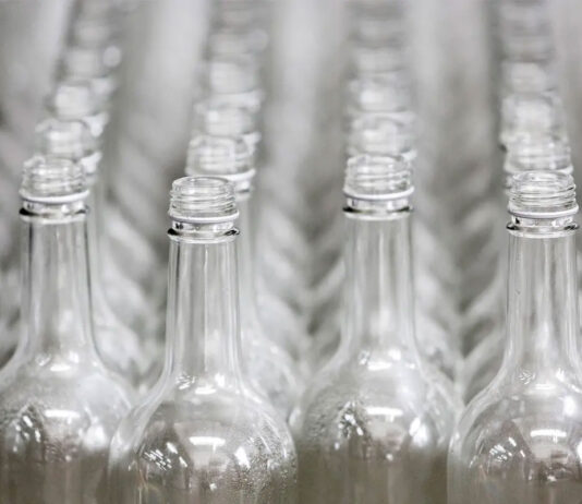 Glass bottle returns permitted under Welsh DRS Rows of glass bottles are lined up on a conveyer belt.