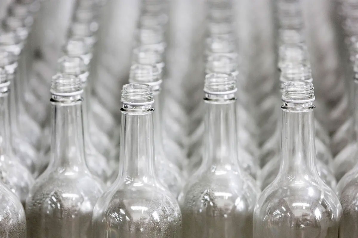 Rows of glass bottles are lined up on a conveyer belt.
