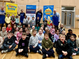 Healthy Living Programme and Scotmid feed over 650 pupils A group of children shout into a camera to mark Brain Health Week with banners for Scotmid Co-op and the Healthy Living Programme behind them.