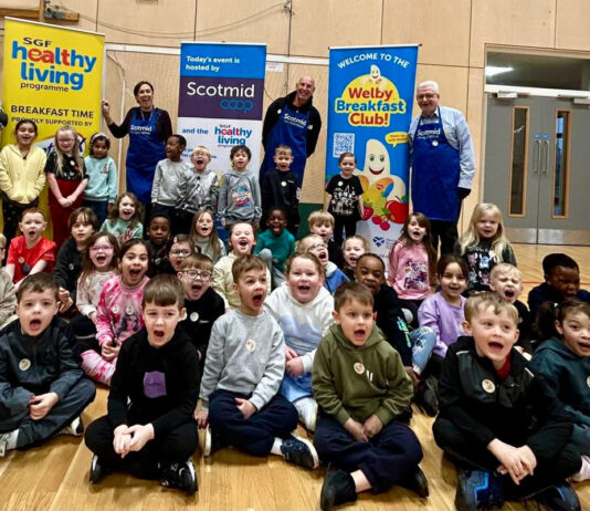 Healthy Living Programme and Scotmid feed over 650 pupils A group of children shout into a camera to mark Brain Health Week with banners for Scotmid Co-op and the Healthy Living Programme behind them.