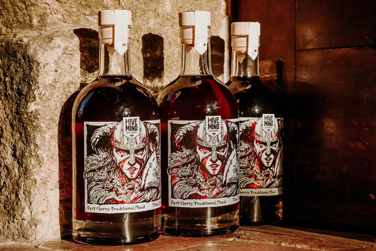 Bottles of Hive Mind Dark Cherry Mead are lined up against a wall.