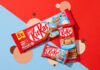 KitKat introduces new Cookie Dough flavour across range Packs of KitKat Cookie Dough formats sit across a red and blue background with beige and brown coloured dots as part of the background design.