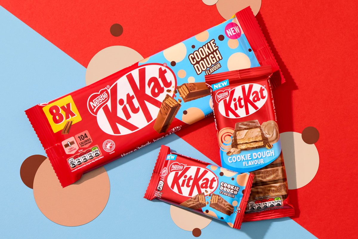 Packs of KitKat Cookie Dough formats sit across a red and blue background with beige and brown coloured dots as part of the background design.