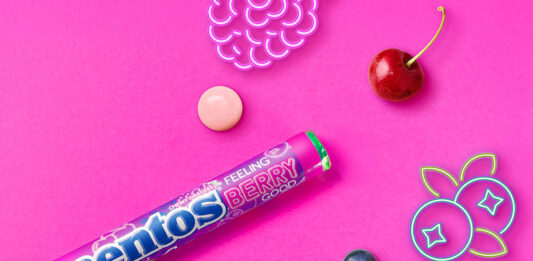Mentos builds impulse sales with Feeling Berry Good single pack Promotional image of launch for Mentos Feeling Berry Good single pack format launch with pack of the sweets with neon signs of fruit with pieces of fruit against a pink background.