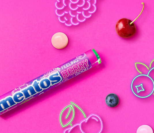 Mentos builds impulse sales with Feeling Berry Good single pack Promotional image of launch for Mentos Feeling Berry Good single pack format launch with pack of the sweets with neon signs of fruit with pieces of fruit against a pink background.