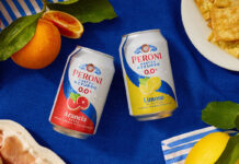 Peroni 0.0% expands alcohol free range with flavoured offer Cans of Peroni 0.0% Arancia Rossa and Limone di Sicilia sit at the middle of a table with a blue tablecloth on top with lemons and blood oranges around the cans and food.